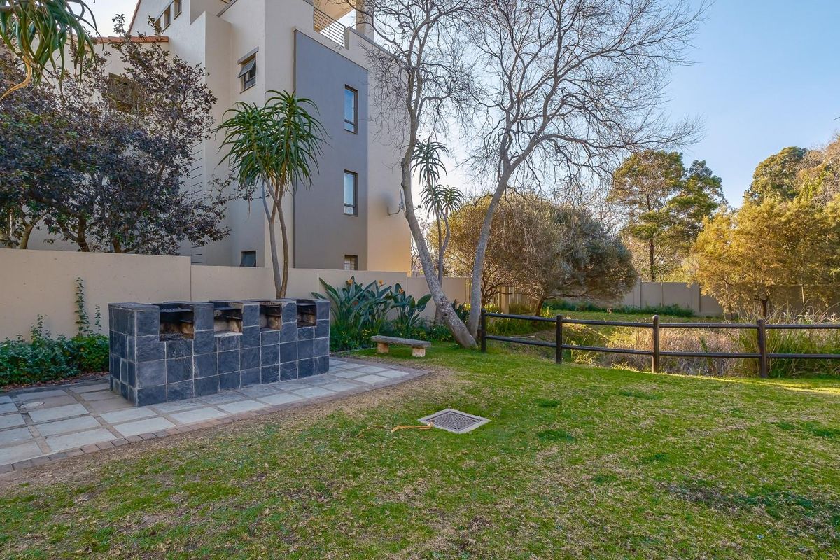 A well-maintained rear garden area featuring a built-in stone braai, paved patio space, and a timber fence overlooking a natural landscape.