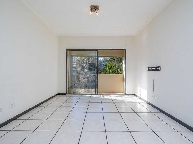 A bright, empty living room featuring tiled flooring and a sliding glass door that opens to an outdoor balcony area.