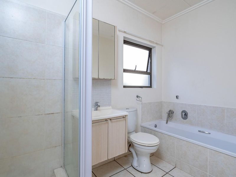 A functional bathroom featuring a separate shower enclosure, bathtub, vanity cabinet with mirror, and tiled finishes throughout.