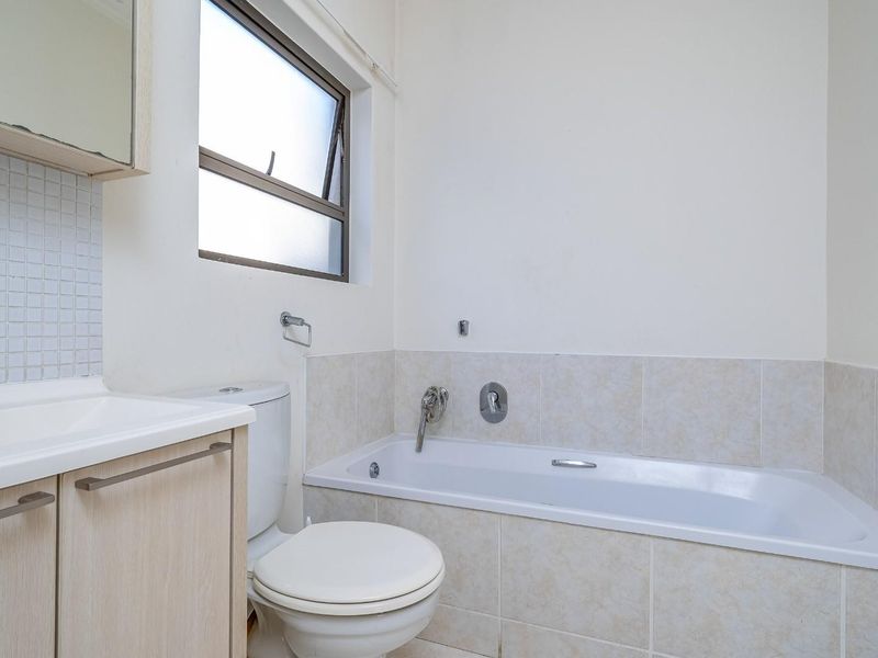 A clean, functional bathroom featuring a built-in vanity, a standard bathtub with tiled surround, and a toilet.