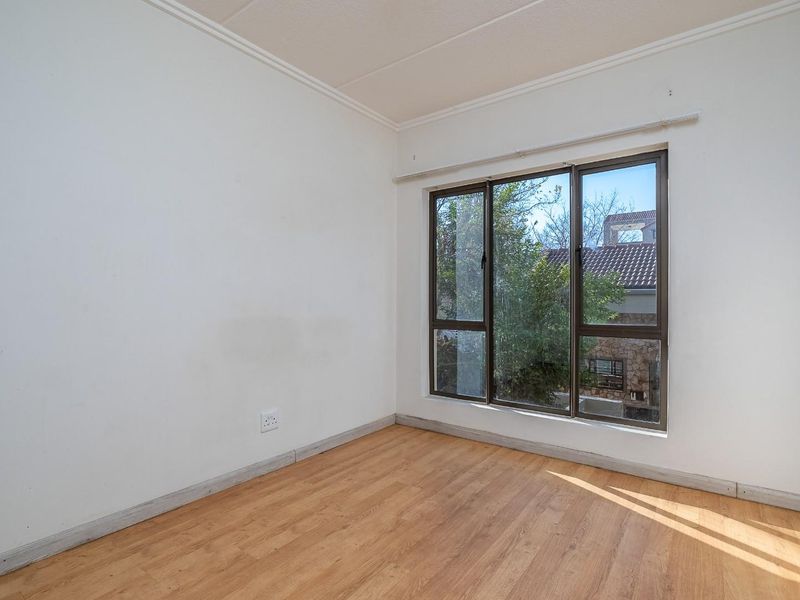 A bright, empty bedroom featuring laminate flooring, neutral walls, and large aluminium-framed windows allowing for natural light.