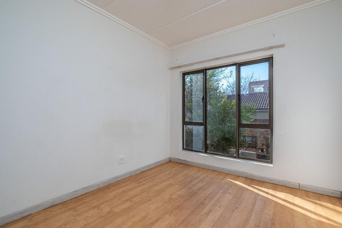 A bright, empty bedroom featuring laminate flooring, neutral walls, and large aluminium-framed windows allowing for natural light.