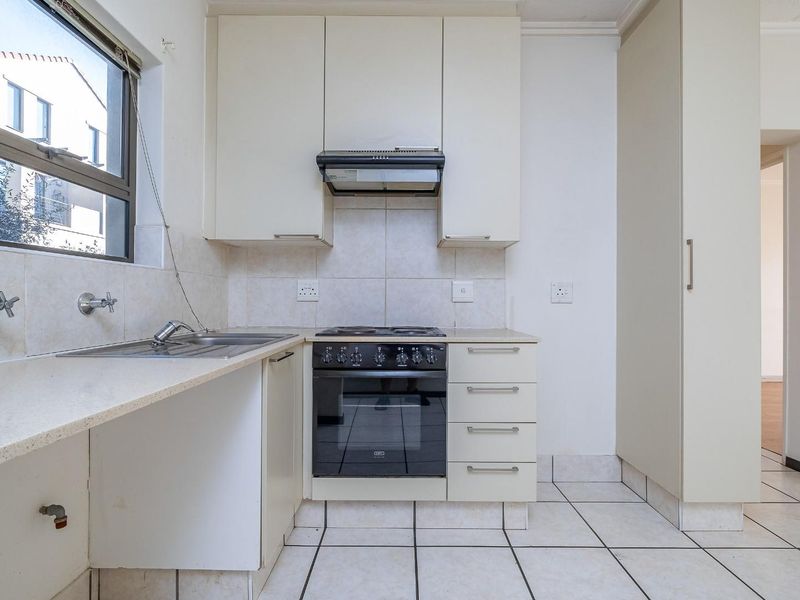 A functional kitchen featuring built-in cabinetry, an electric stove with oven, extractor fan, and tiled flooring. The space is clean and ready for updates.