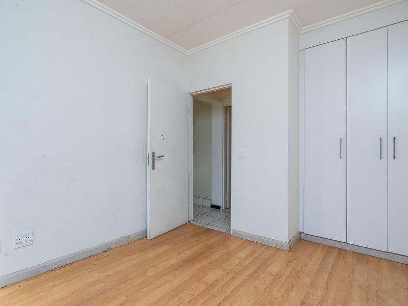 A bright, empty bedroom featuring light laminate flooring, white walls, and built-in storage cupboards with a neutral finish.