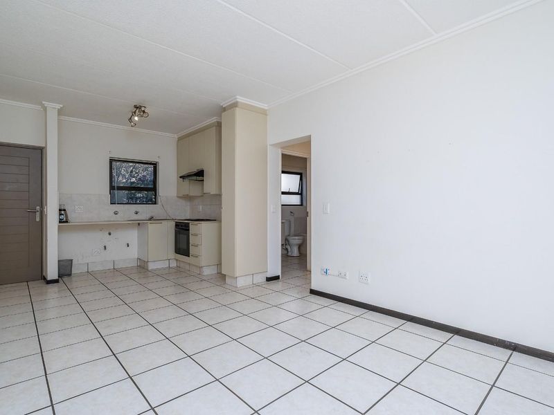 An open-plan living and kitchen area featuring tiled flooring, built-in cabinetry, and an integrated oven, presenting a blank canvas for renovation.