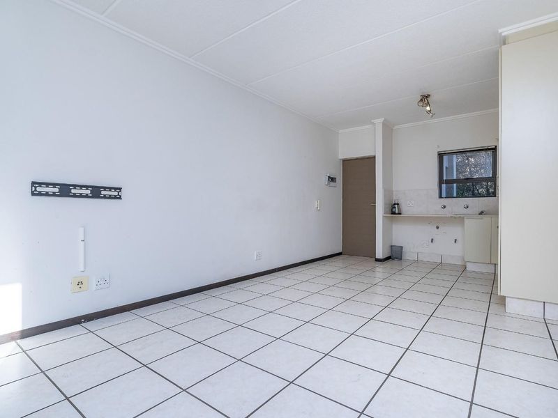 An empty open-plan living and kitchen area featuring tiled flooring, built-in cabinetry, and a functional sink, offering a blank canvas for renovation.