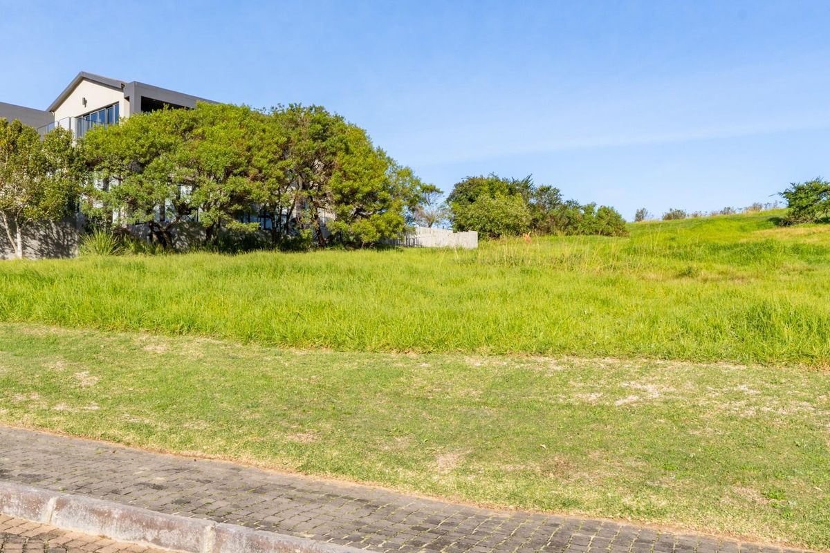 A vacant residential plot featuring established grass and a paved verge, situated in a developed neighborhood setting.