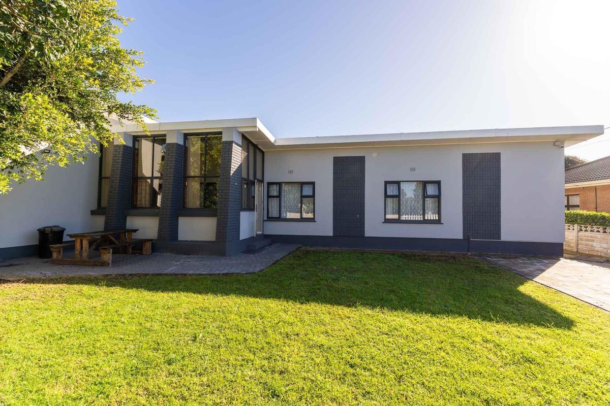 Rear view of the house featuring a paved patio area, well-maintained lawn, and modern grey-painted brick exterior with dark aluminium window frames.