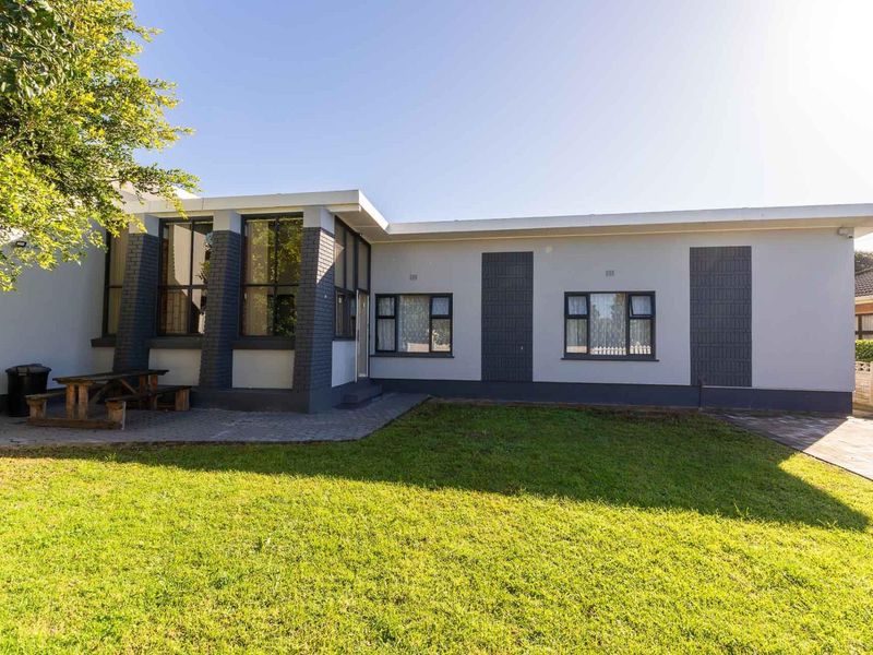 Rear view of the house featuring a paved patio area, well-maintained lawn, and modern grey-painted brick exterior with dark aluminium window frames.