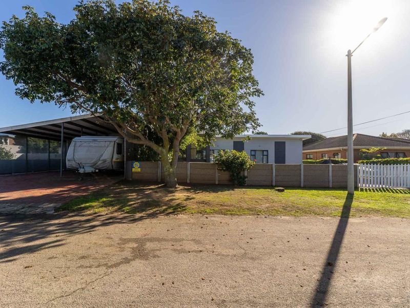 Front exterior view of the property featuring a paved driveway, carport, and secure boundary walling with a white picket gate.