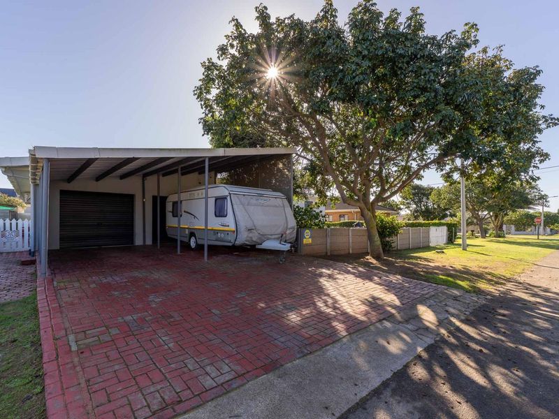 Front exterior view featuring a paved driveway, a covered carport, and a secure boundary wall with a pedestrian gate.