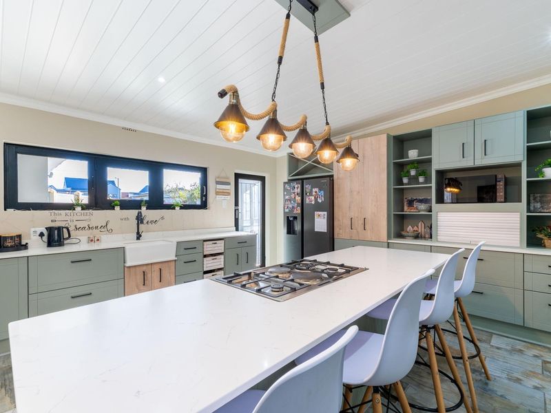 Modern kitchen featuring a large island with a built-in gas cooktop, sage green cabinetry, apron-front sink, and stylish pendant lighting.