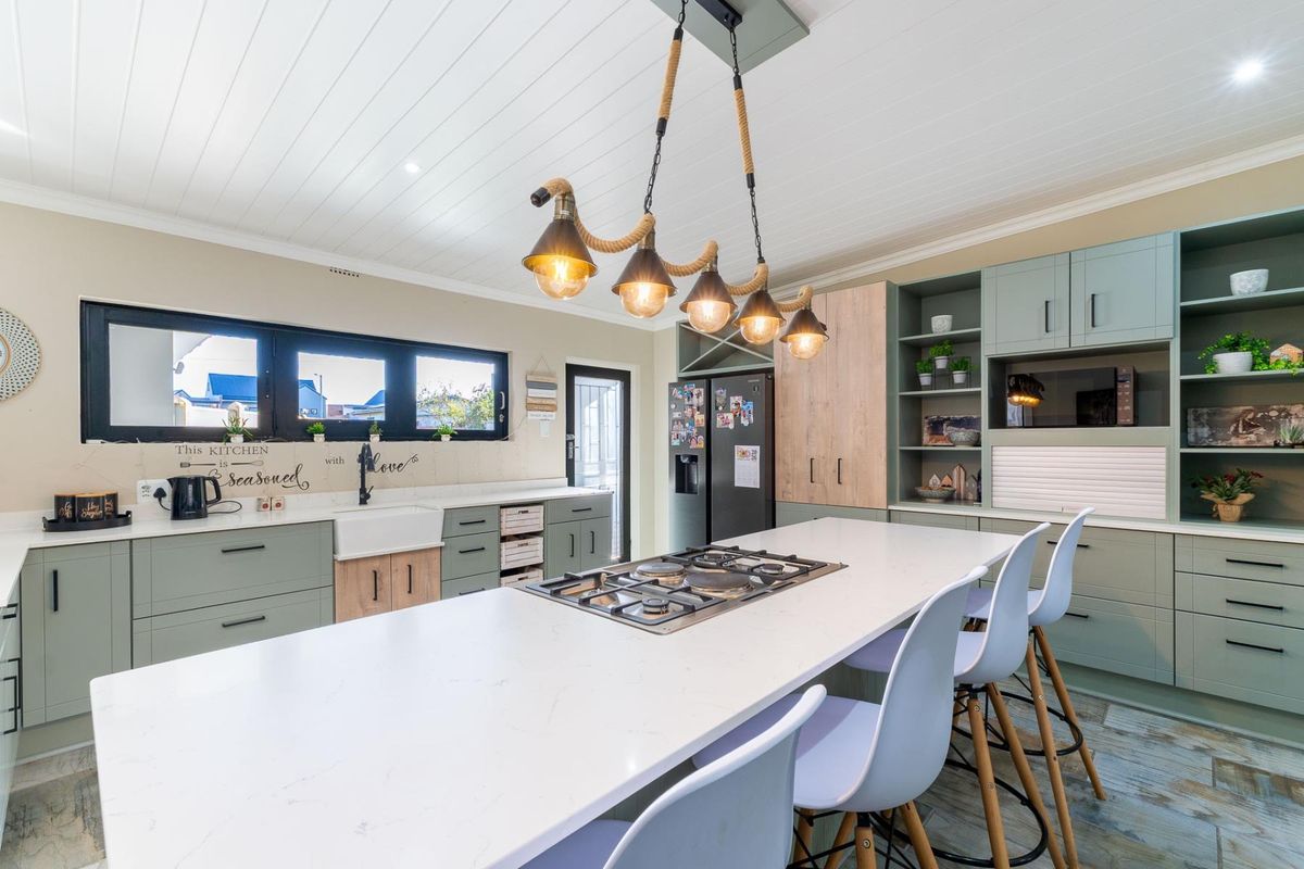 Modern kitchen featuring a large island with a built-in gas cooktop, sage green cabinetry, apron-front sink, and stylish pendant lighting.