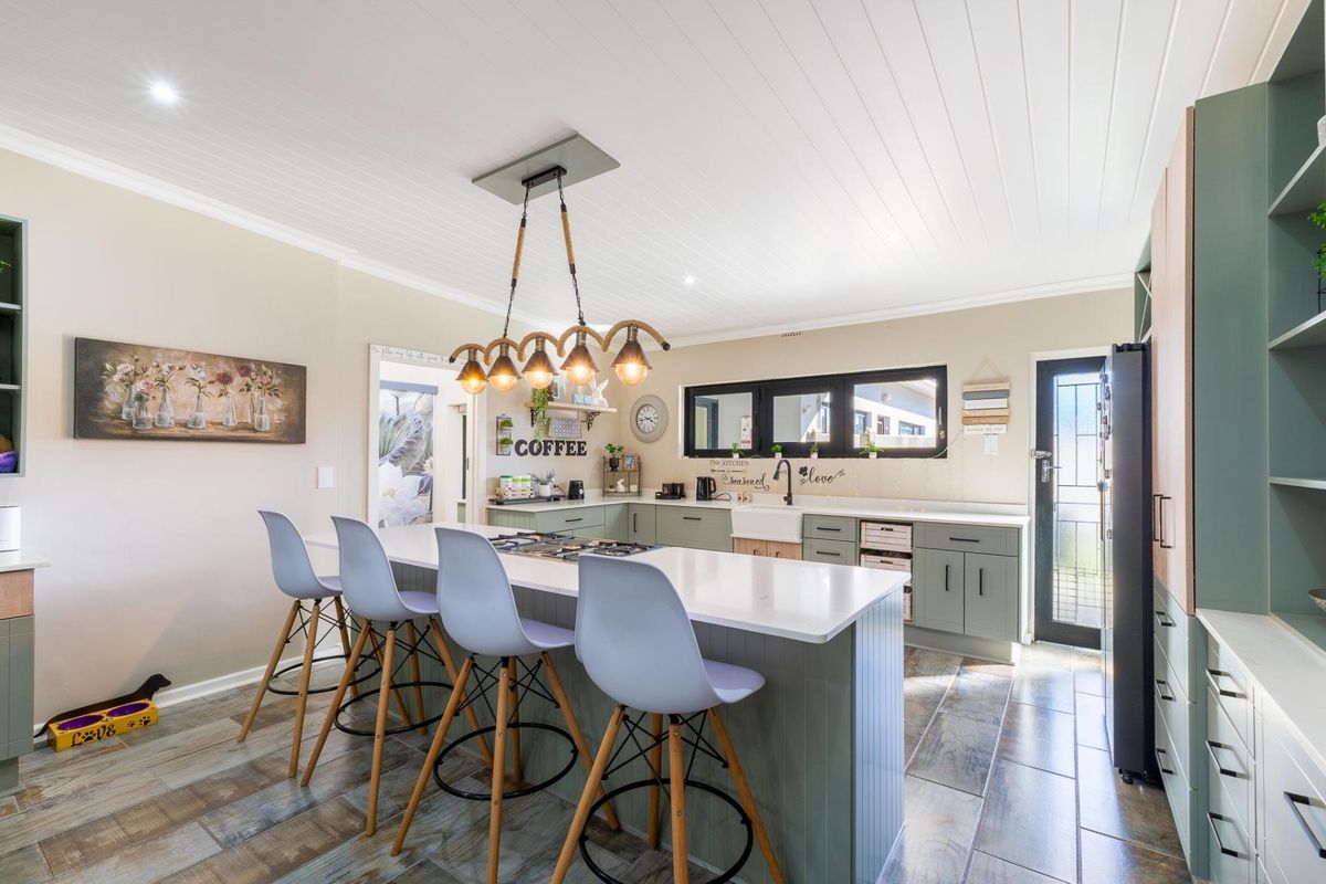 Modern kitchen featuring a large island with stone countertops, farmhouse sink, sage green cabinetry, and a stylish tongue and groove ceiling.