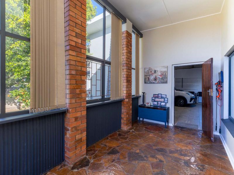 A sunroom or enclosed patio featuring exposed brick pillars, flagstone flooring, and large windows providing natural light, with direct access to the garage.