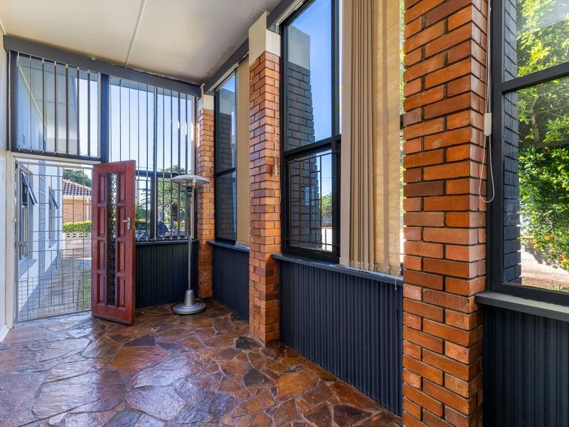 A covered patio area featuring flagstone flooring, exposed brick pillars, and large windows, providing a bright and secure transition space to the outdoors.