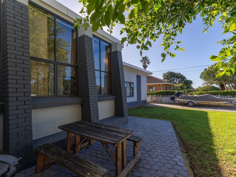 A rear exterior view featuring a paved patio area, dark brick architectural detailing, large windows, and a well-maintained lawn.