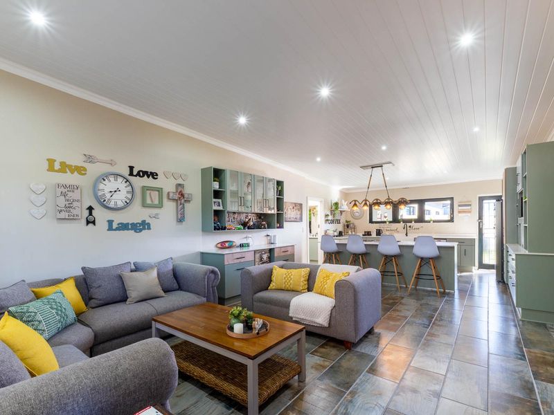 Spacious open-plan living and kitchen area featuring a large island, integrated cabinetry, modern downlights, and durable stone tile flooring throughout.