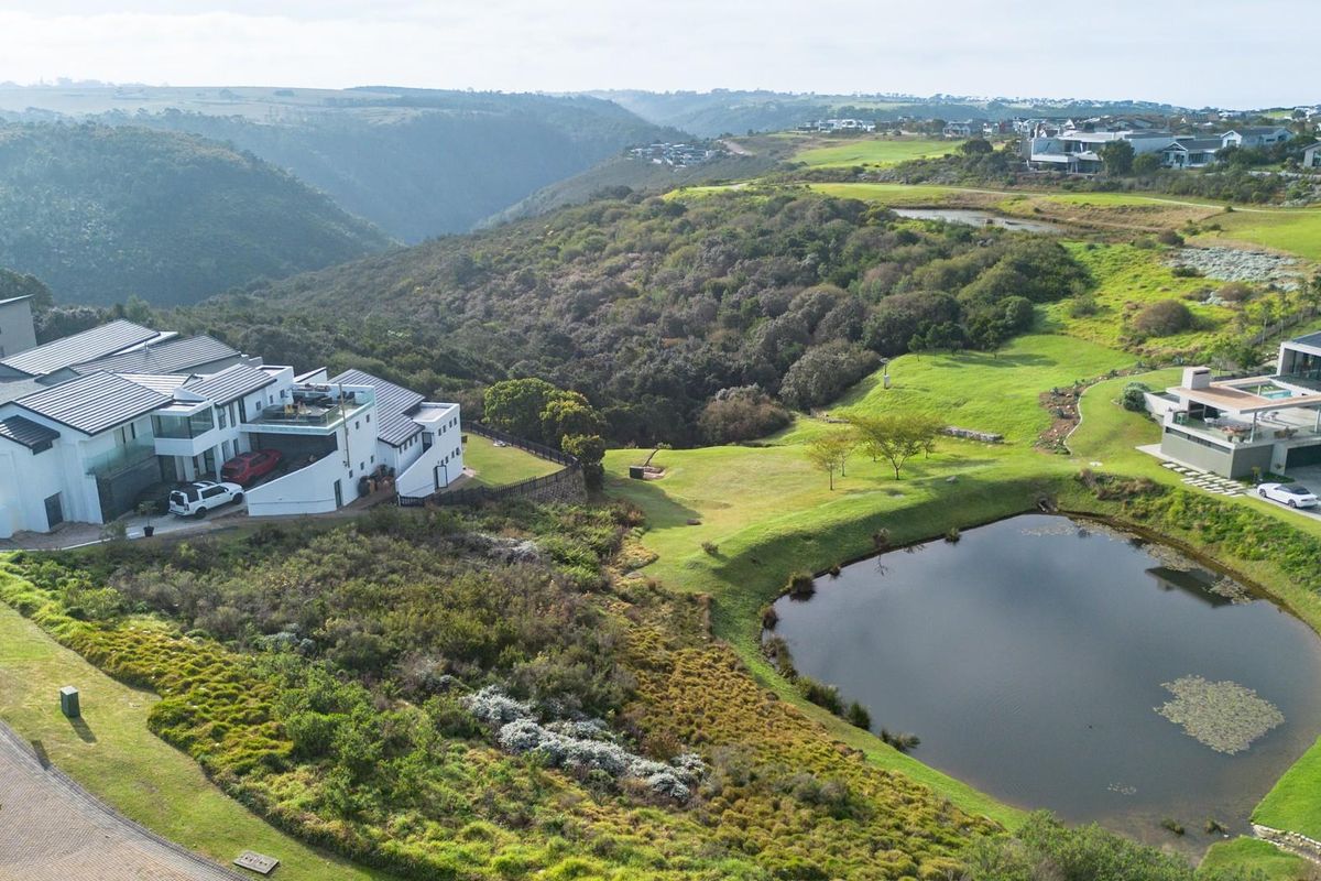 Aerial view of a residential estate featuring landscaped grounds, a natural pond, and surrounding hilly terrain.