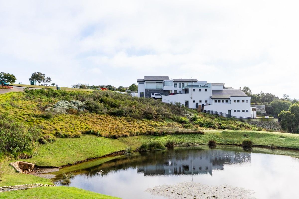 An elevated view of a residential property featuring a landscaped garden and a natural pond in the foreground.