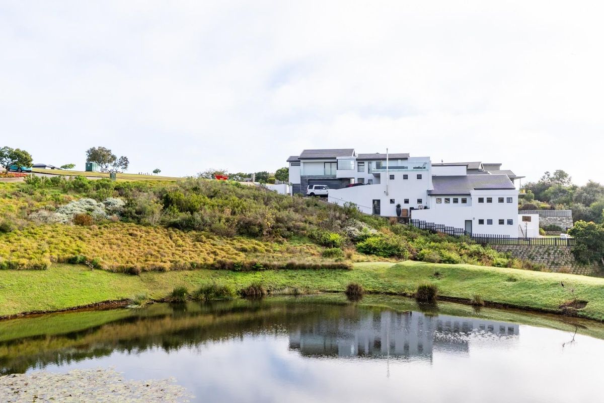 A view of the rear elevation of a modern residential property overlooking a landscaped garden and a natural pond.