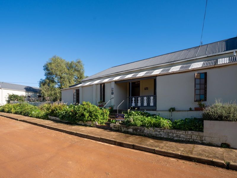 Front elevation of a traditional house featuring a corrugated metal roof, a covered veranda, and a stone retaining wall along the street frontage.