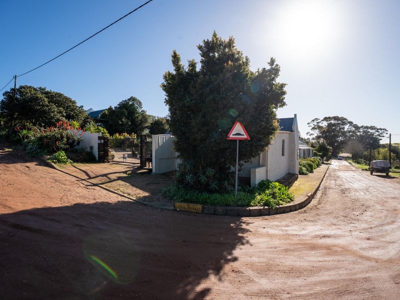 A street-level view showing the property entrance, boundary wall, and metal gate from the unpaved road.