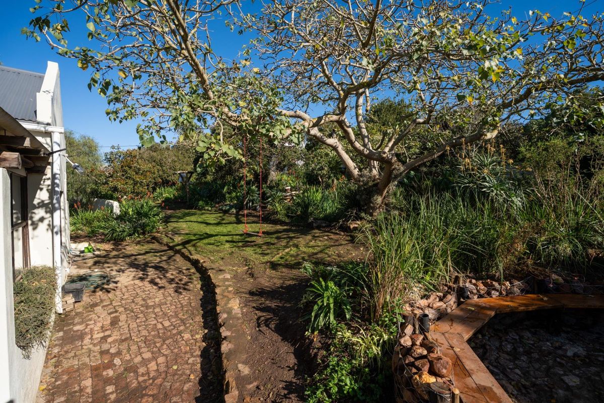 A private rear garden featuring mature trees, established landscaping, brick paved pathways, and a stone-retained garden bed.
