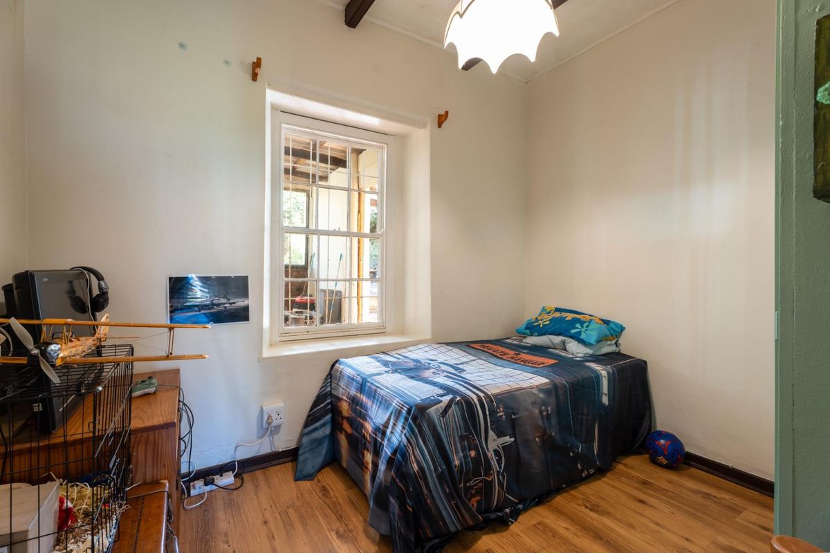 A compact bedroom featuring laminate flooring, a timber-framed window with security bars, and an exposed ceiling beam.