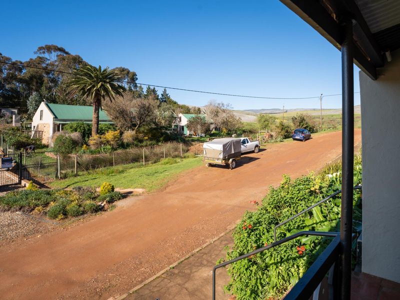 A view from an elevated position overlooking a rural dirt road, surrounding landscape, and neighboring properties.