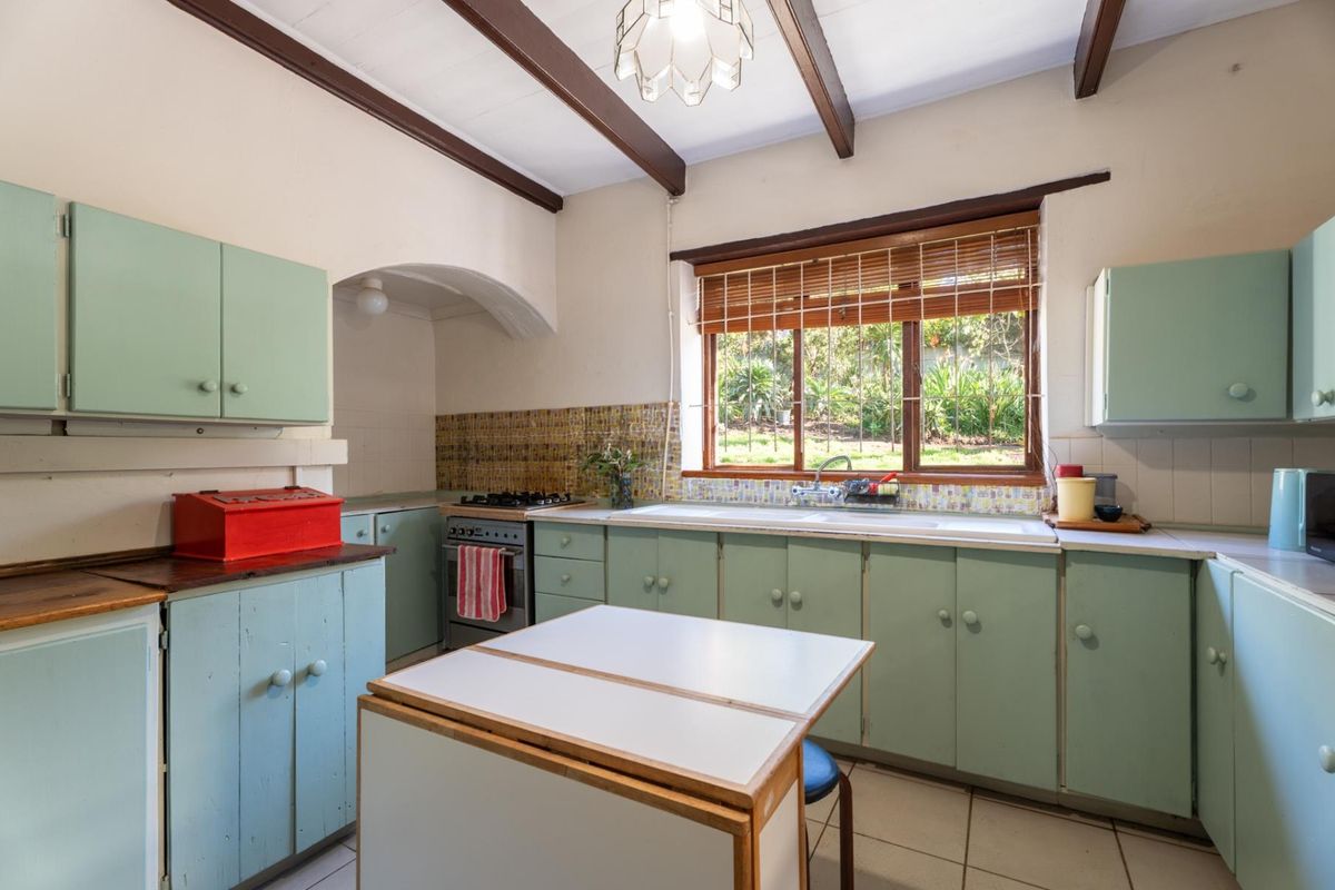 A functional kitchen featuring vintage-style cabinetry, exposed timber ceiling beams, a gas hob, and a double basin sink overlooking the garden.