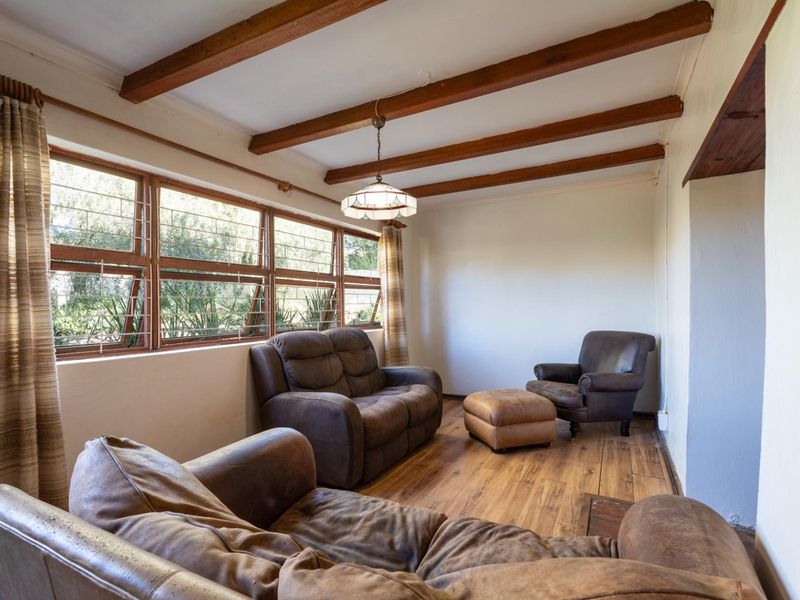 A living room featuring exposed timber ceiling beams, laminate flooring, and large timber-framed windows with security bars, offering a rustic and cozy atmosphere.