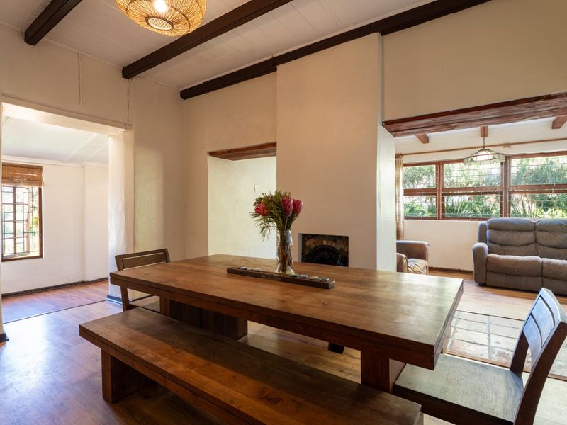 Open-plan living and dining area featuring exposed timber ceiling beams, warm timber flooring, and a central built-in fireplace.