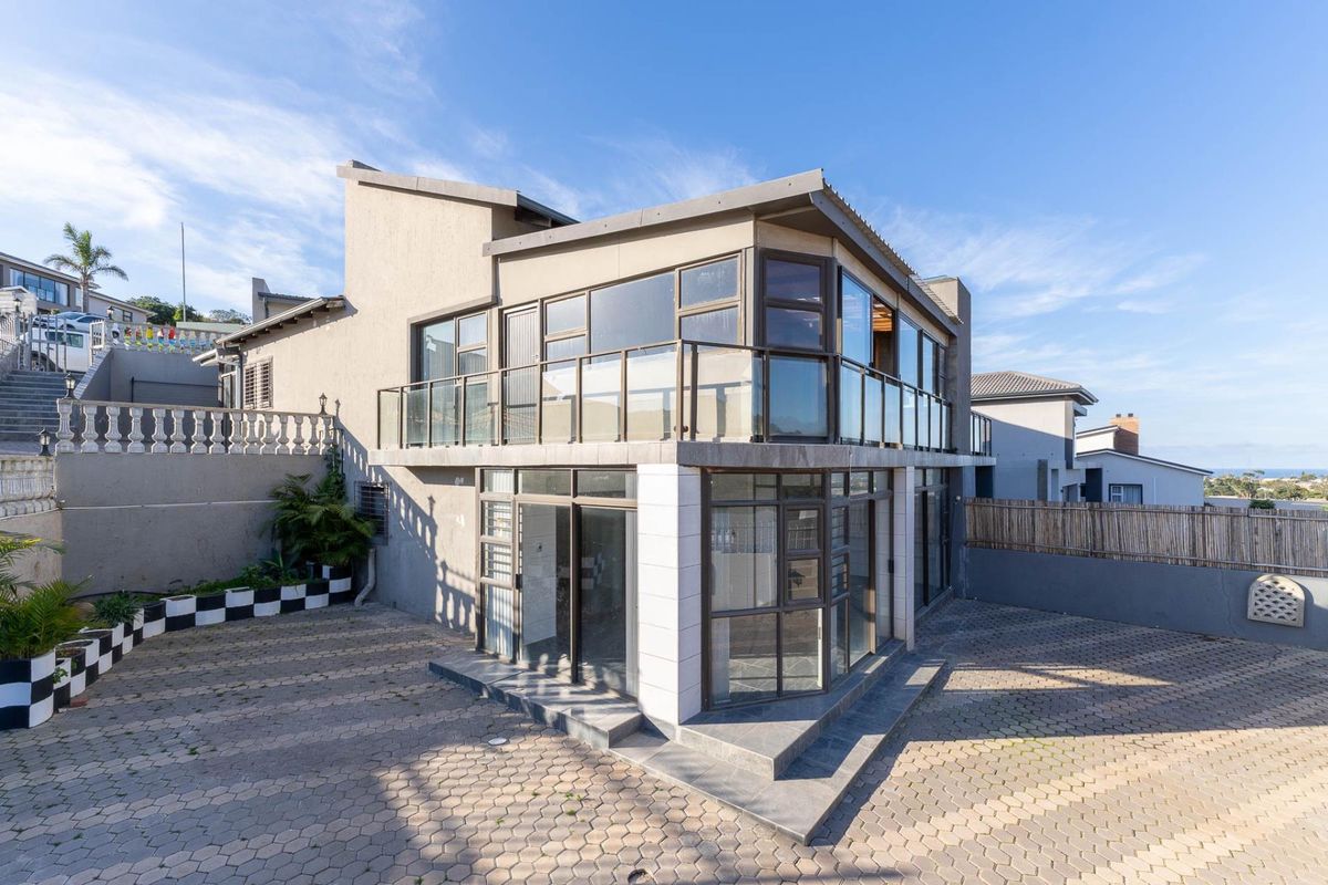 Rear exterior view of a modern townhouse featuring a paved driveway, large glass windows, and an upper-level balcony with a glass balustrade.
