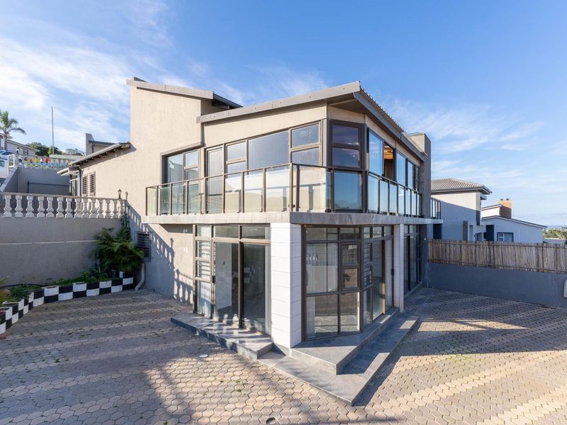 Rear exterior view of a modern townhouse featuring a paved driveway, large glass windows, and an upper-level balcony with a glass balustrade.