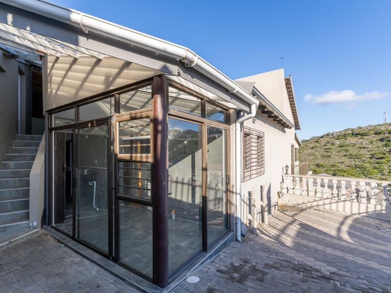 An enclosed patio area featuring sliding glass doors, paved flooring, and stone stairs, offering a versatile outdoor space with views of the surrounding landscape.