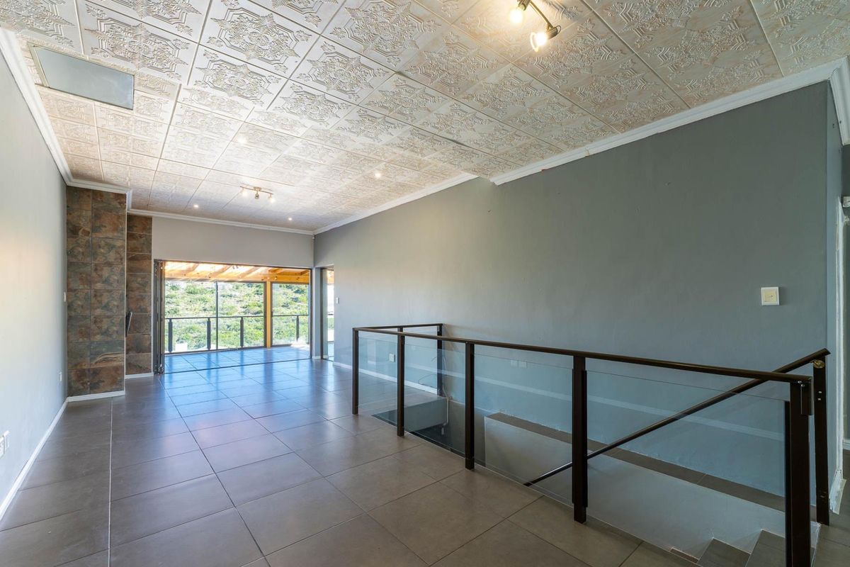 Spacious open-plan living area featuring decorative ceiling tiles, large format floor tiles, a stone feature wall, and a modern glass balustrade overlooking the staircase.