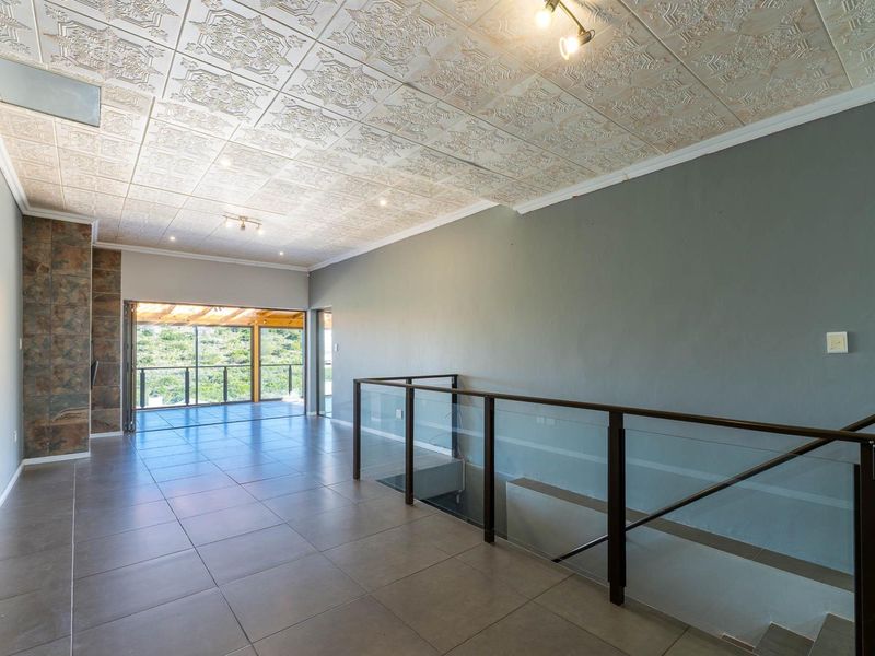 Spacious open-plan living area featuring decorative ceiling tiles, large format floor tiles, a stone feature wall, and a modern glass balustrade overlooking the staircase.