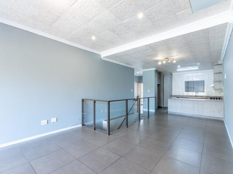 Spacious open-plan living area featuring tiled flooring, a modern glass balustrade, and an integrated kitchen with built-in cabinetry and appliances.