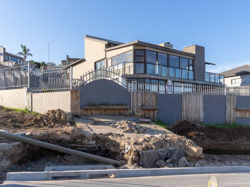 Front exterior view of a modern townhouse featuring large glass windows and a balcony, currently undergoing exterior landscaping and driveway construction.