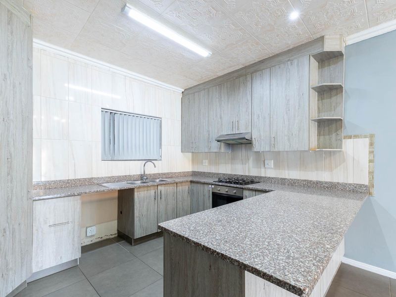 A functional kitchen featuring granite countertops, built-in cabinetry, a gas hob, and an integrated oven, offering a clean and practical workspace.