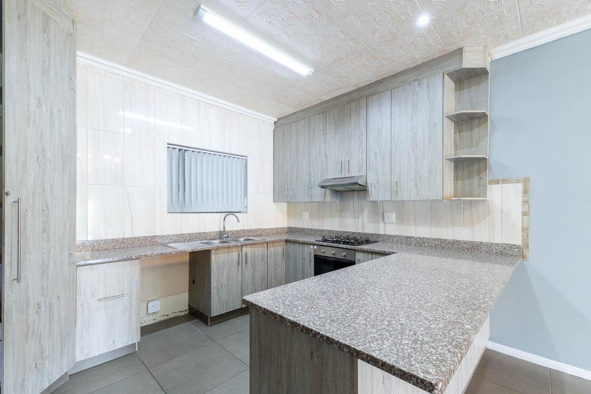 A functional kitchen featuring granite countertops, built-in cabinetry, a gas hob, and an integrated oven, offering a clean and practical workspace.