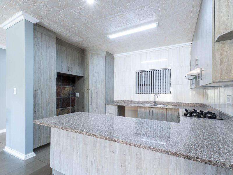 A functional kitchen featuring granite countertops, built-in cabinetry, a gas hob with extractor fan, and tiled finishes throughout.
