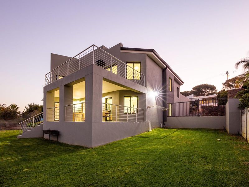 Rear view of a modern two-story house featuring a covered patio, upper balcony with stainless steel railings, and a well-maintained lawn.
