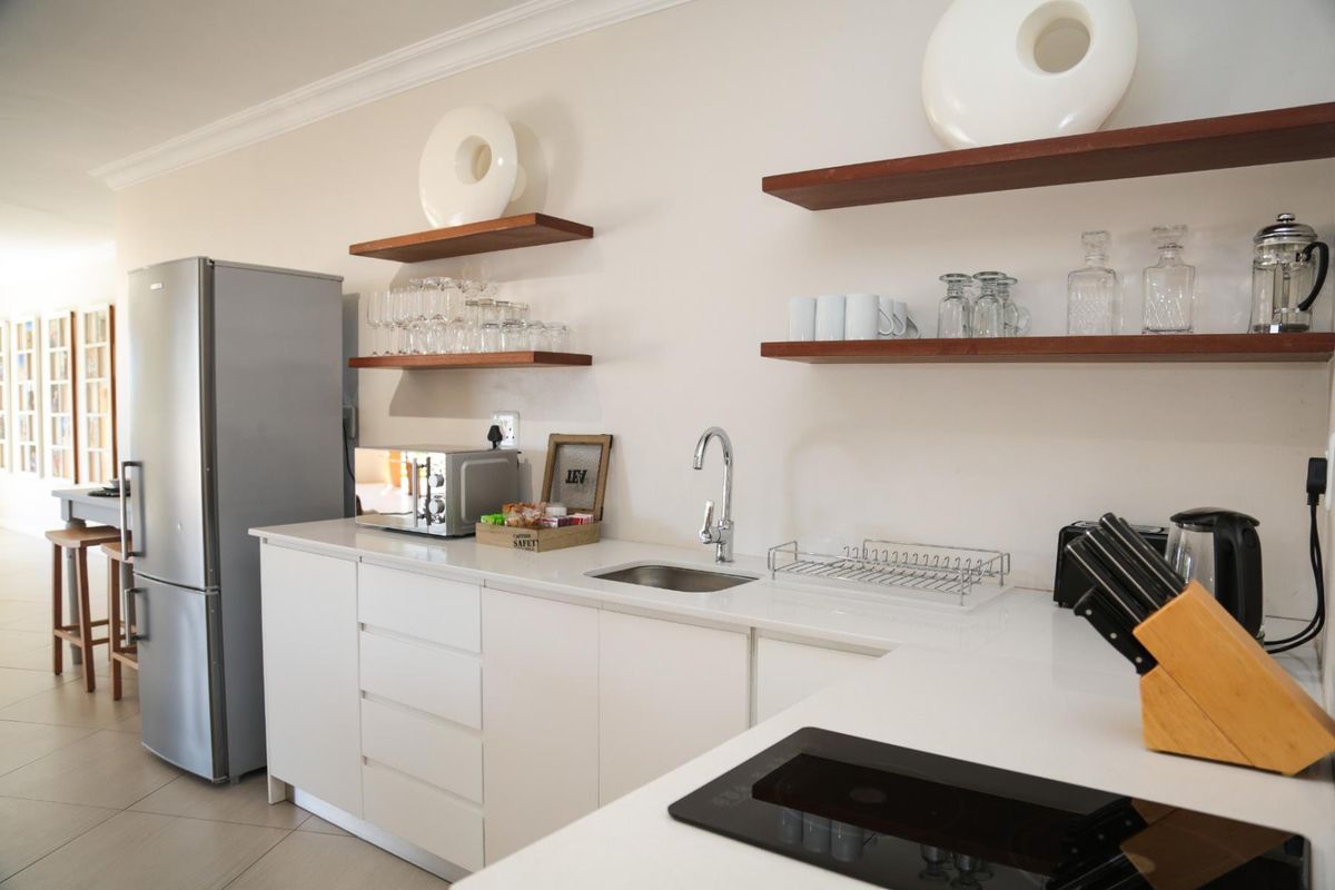 Modern kitchen featuring white cabinetry, stone countertops, floating timber shelving, and a built-in induction hob, offering a clean and functional workspace.