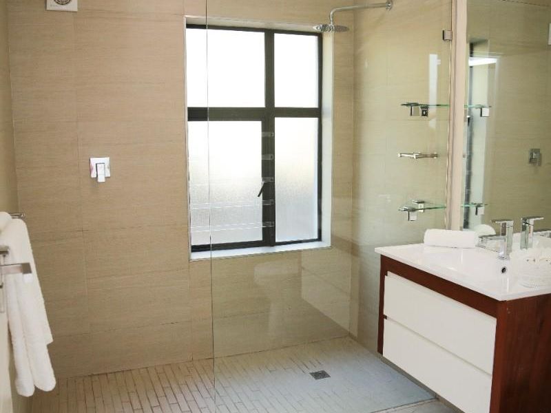 Modern bathroom featuring a walk-in shower with glass screen, wall-mounted vanity with basin, and neutral floor-to-ceiling tiling.