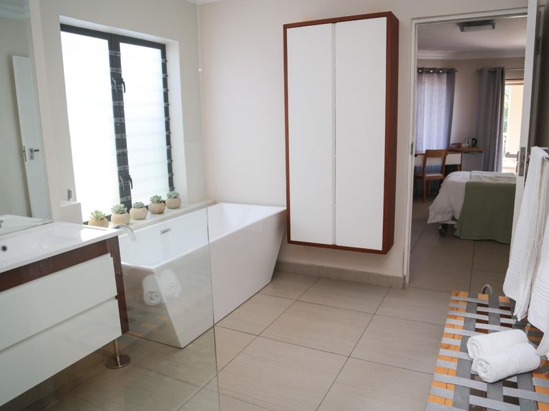 Modern bathroom featuring a sleek freestanding bathtub, contemporary vanity, wall-mounted storage, and neutral floor tiling with a view into the adjacent bedroom.