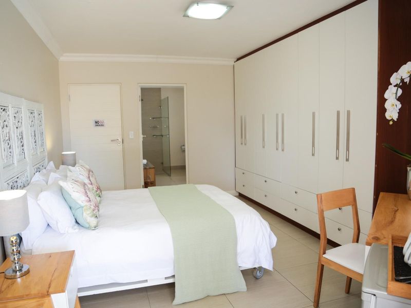 Spacious bedroom featuring extensive built-in cupboards, neutral tiled flooring, and direct access to an en-suite bathroom.