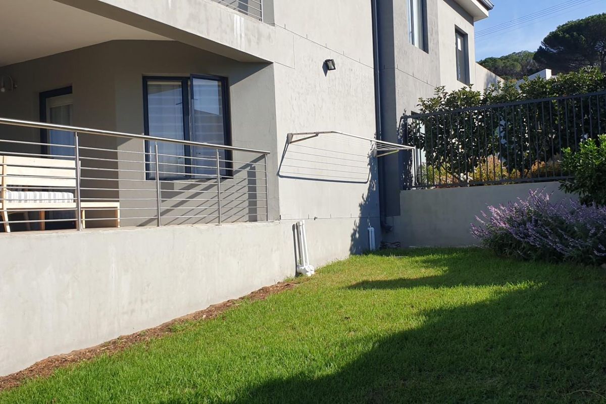 A well-maintained rear garden area featuring a lawn, perimeter fencing, and a covered patio with a stainless steel balustrade.