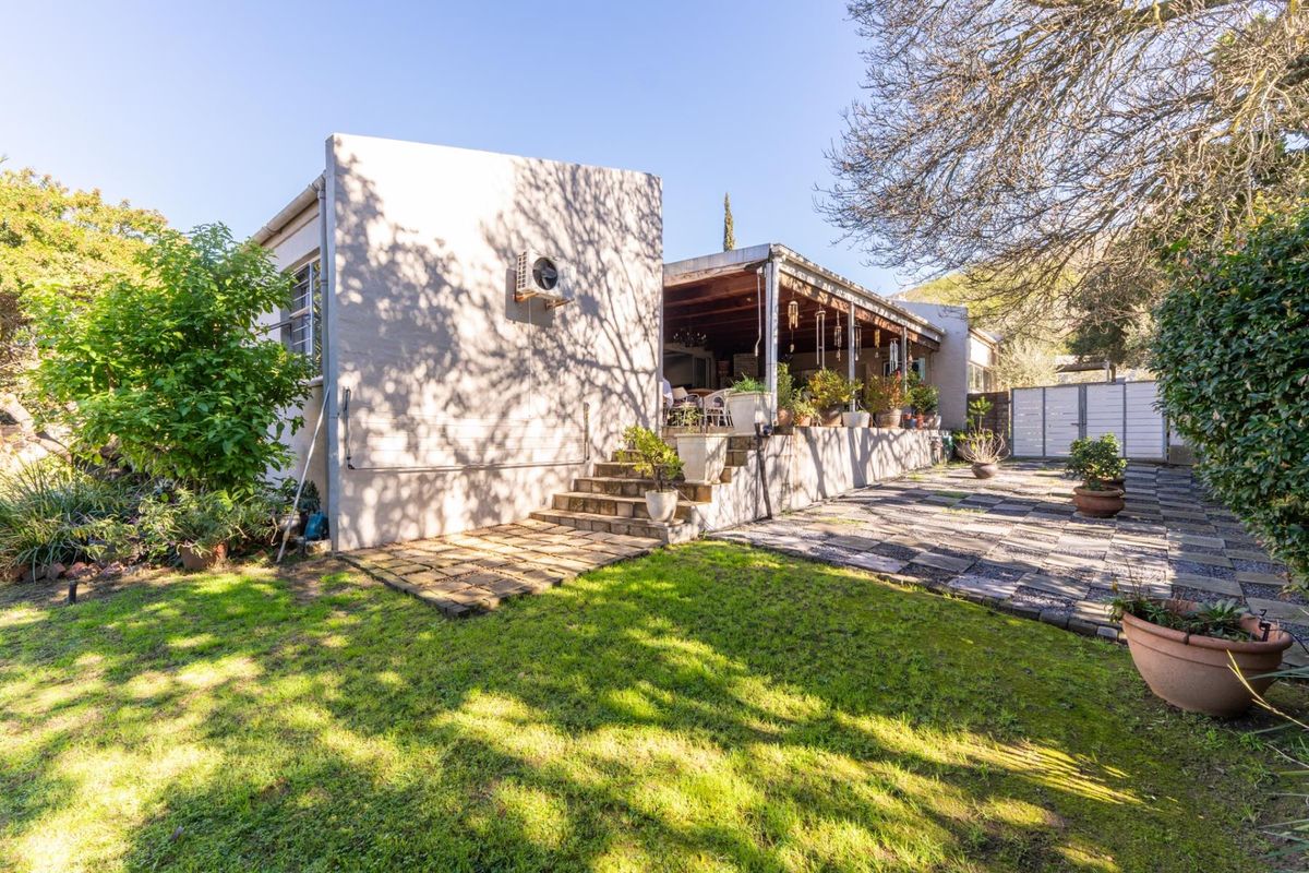 Rear view of the property featuring a covered patio, stone paved area, and a well-maintained garden lawn.